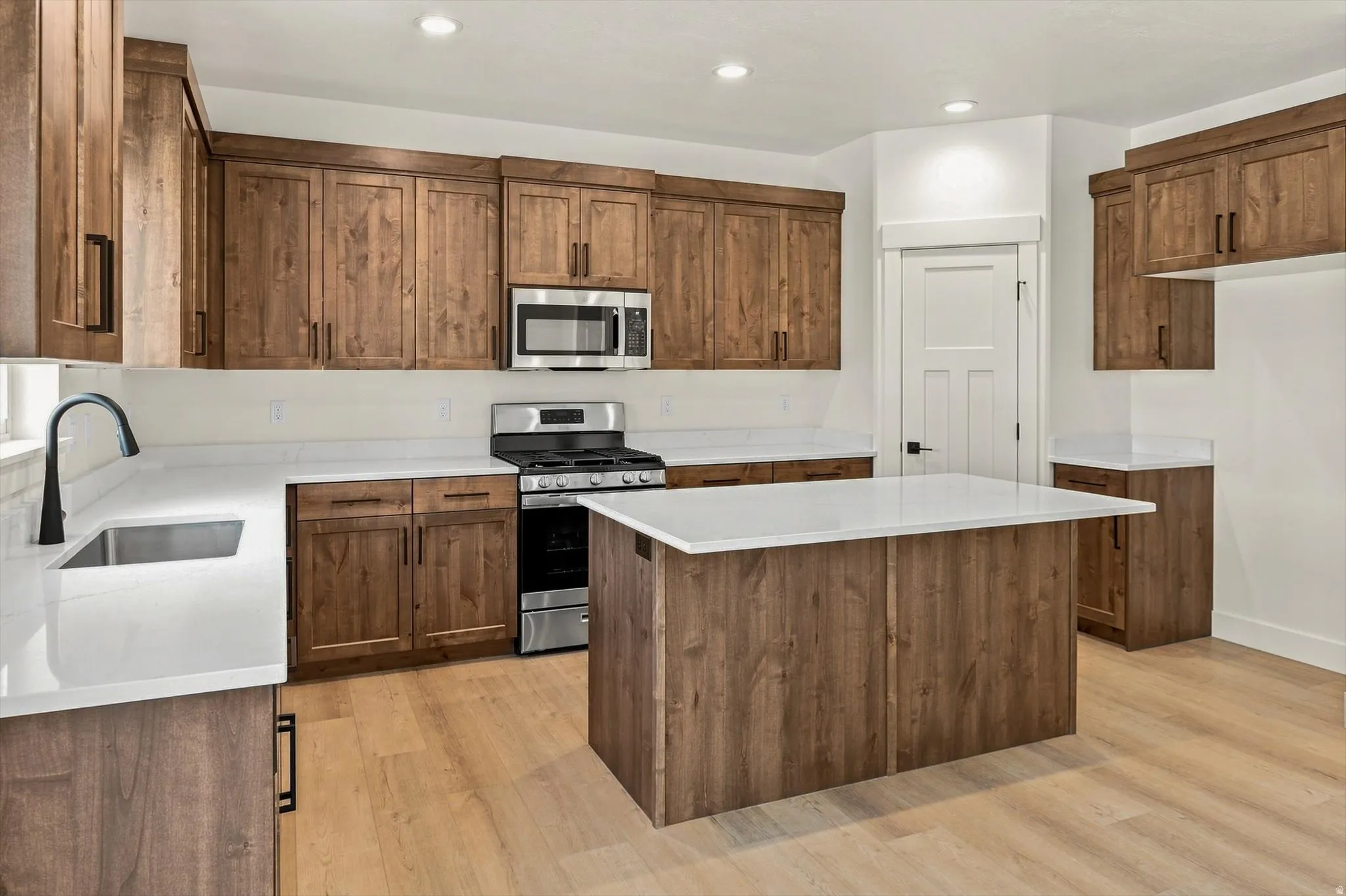 Kitchen featuring wood-finish cabinetry, light-toned countertops, a central island, stainless steel appliances, and wood-finish flooring