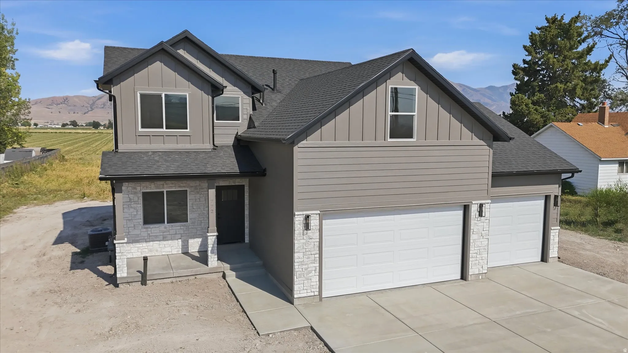 Modern two-story residence featuring a gray exterior, white stone accents, a dark asphalt shingle roof, a two-car garage, and a concrete driveway