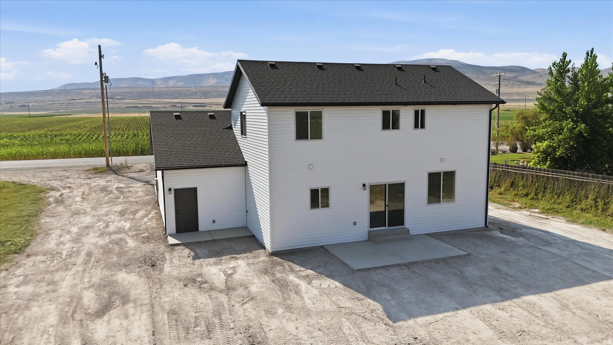 White siding exterior with a black shingle roof, featuring a concrete patio and a single-story attached structure with a separate entrance