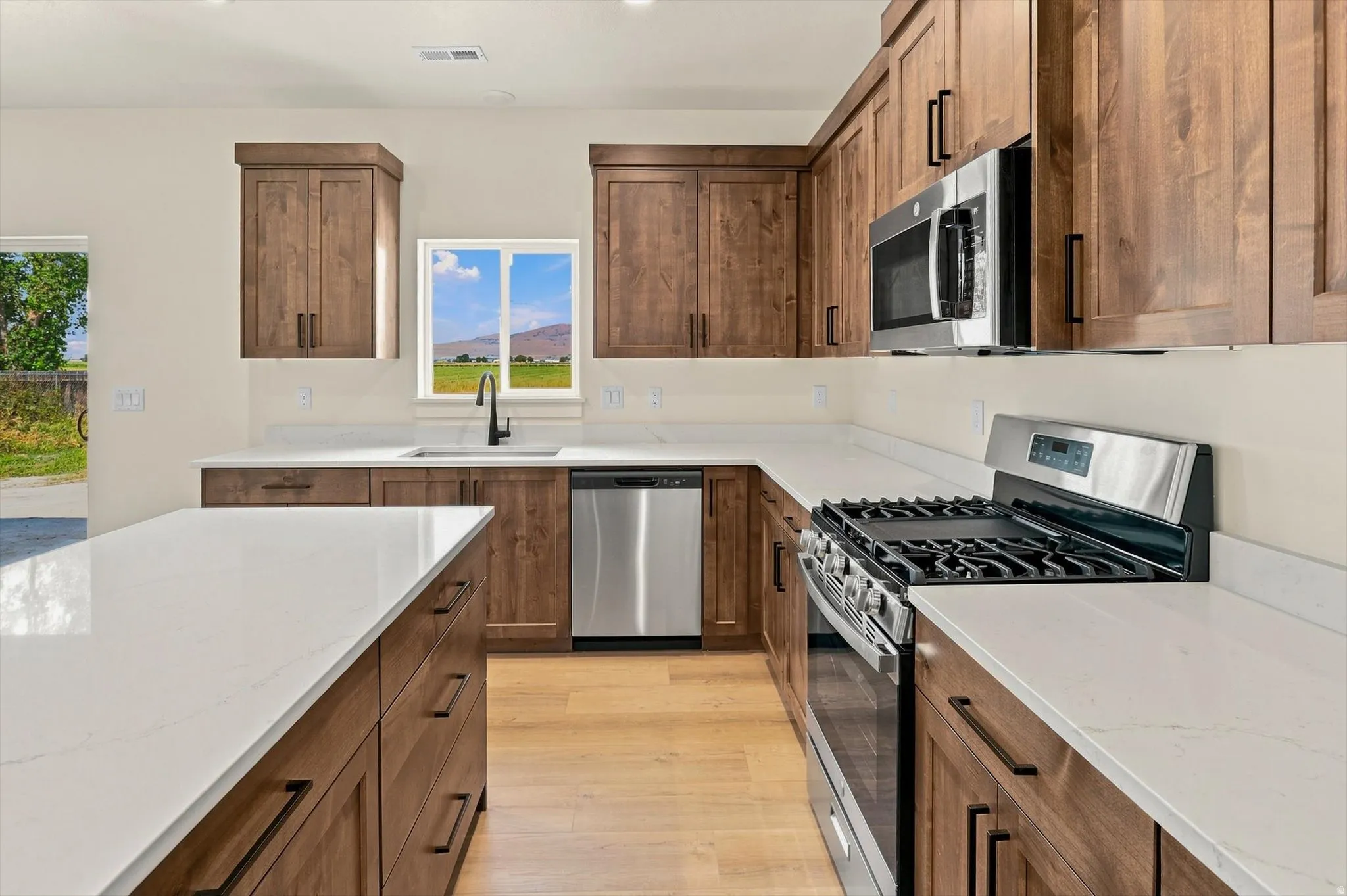 Kitchen featuring wood-finish cabinetry, stainless steel appliances, white countertops, and wood-finish flooring