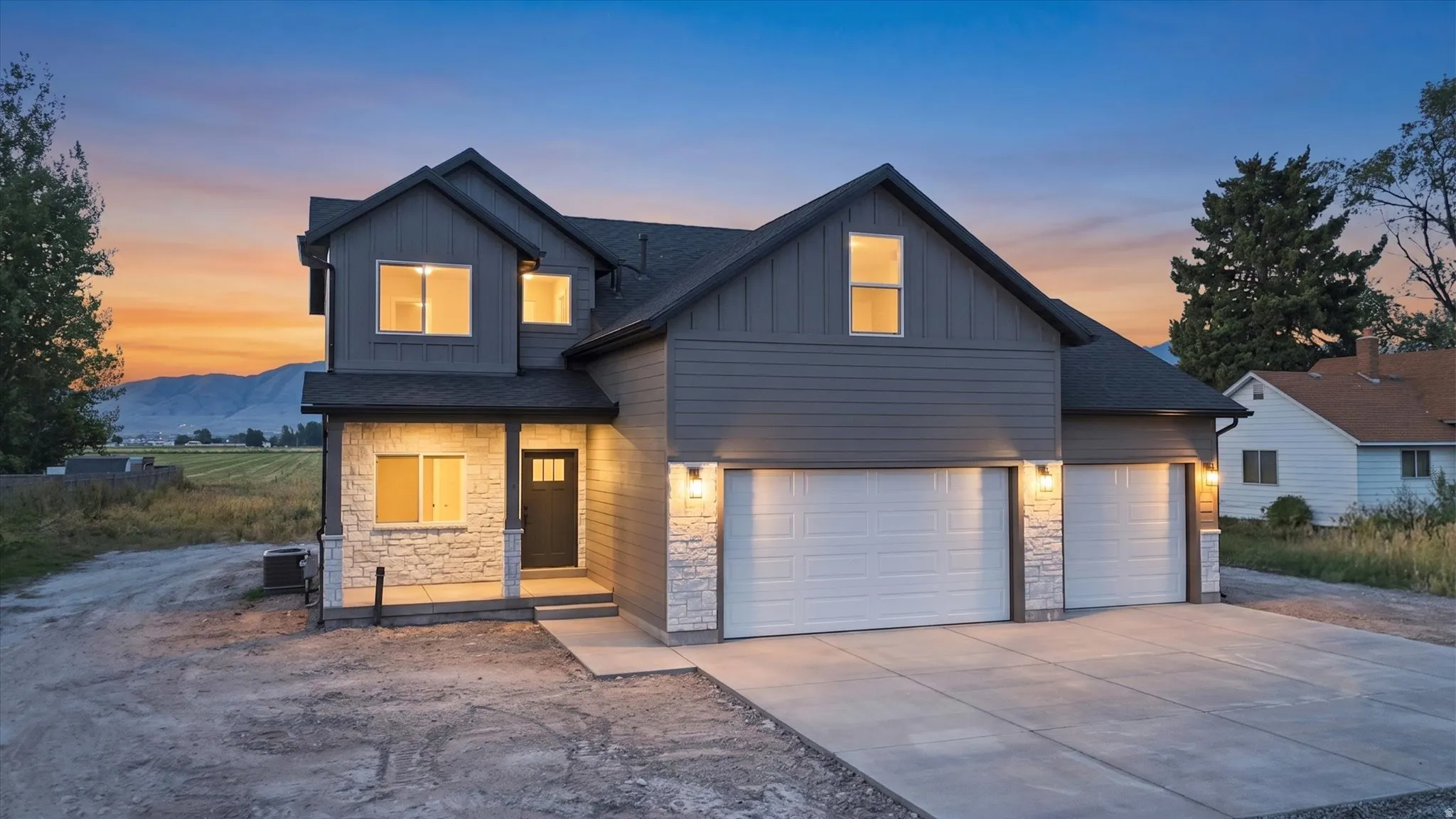 Contemporary exterior with stacked stone accents, dark siding, an inviting front porch, and an attached three-car garage