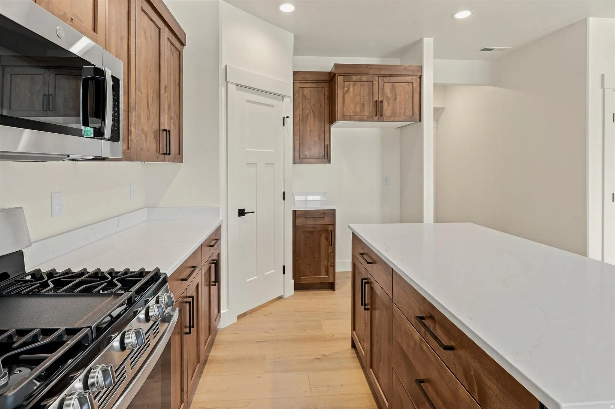 Kitchen featuring hardwood-finish flooring, recessed lighting, wood cabinetry, stainless steel appliances, and light-toned countertops