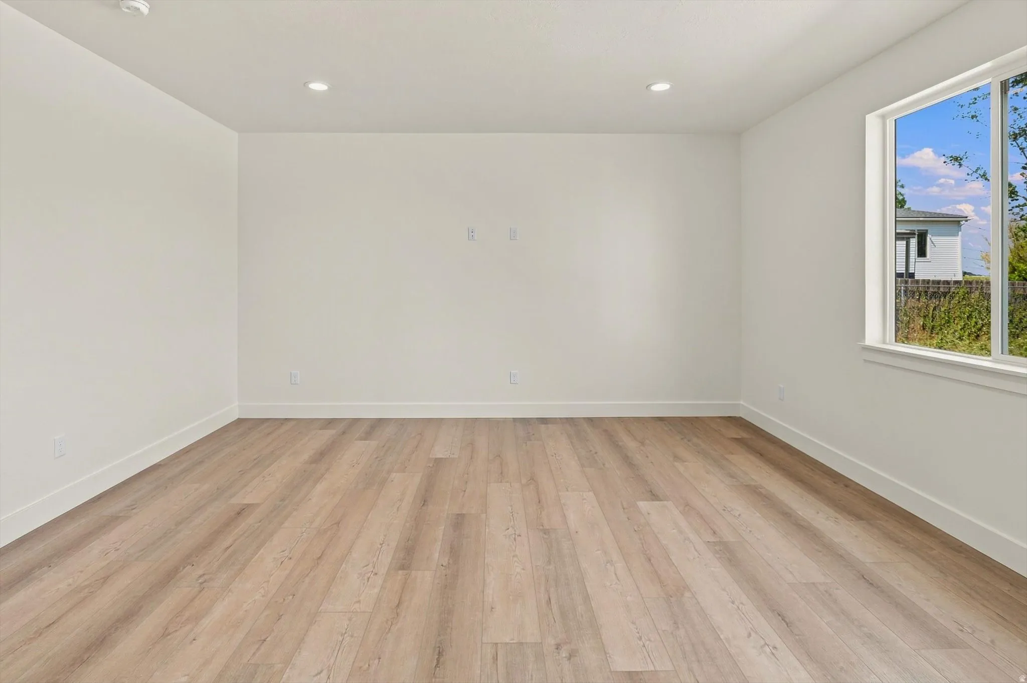 Recessed ceiling lighting, wood-finish flooring, white walls, and a large window