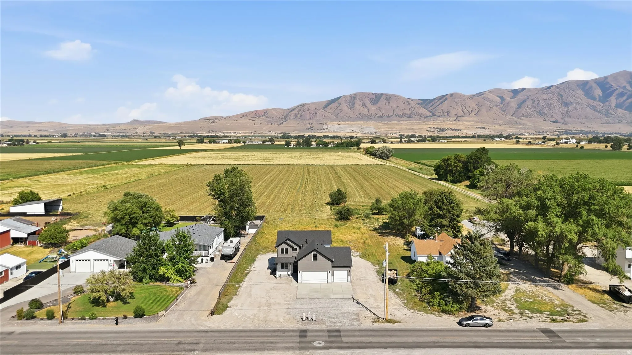 Contemporary-style residence with an attached two-car garage, featuring a gravel driveway and a surrounding open landscape with distant mountains