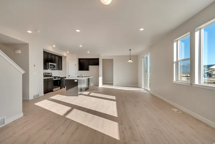 Open-concept living space with light wood-finish flooring, recessed lighting, and a modern kitchen featuring dark cabinetry and an island. *Not actual home. Buyer will choose their own cabinets, counters, and fixtures.