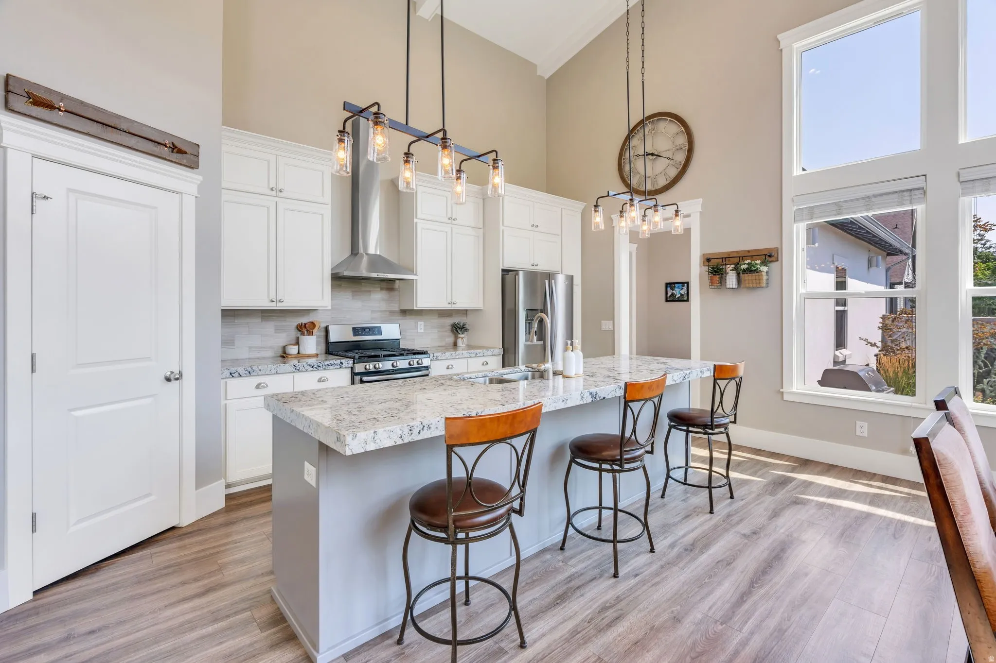 Kitchen featuring high ceilings, wood-finish flooring, white cabinetry, a central island with countertop seating, and large windows
