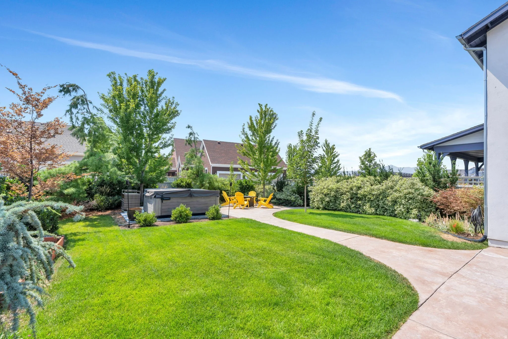 Expansive backyard featuring a manicured lawn, established landscaping, and a paver patio with a built-in spa