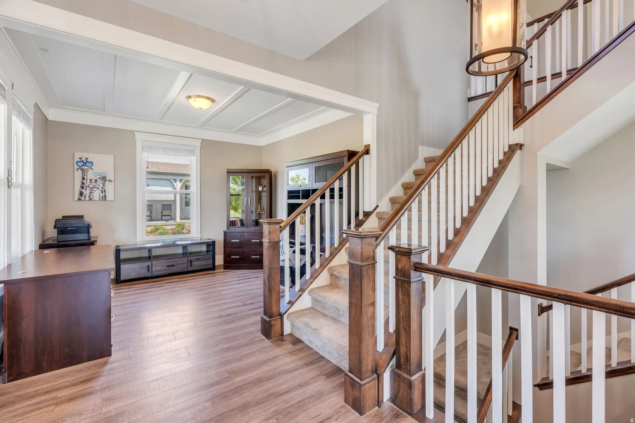 Wood-finish flooring throughout, a coffered ceiling with recessed lighting, and a grand staircase with white balusters and wood handrails
