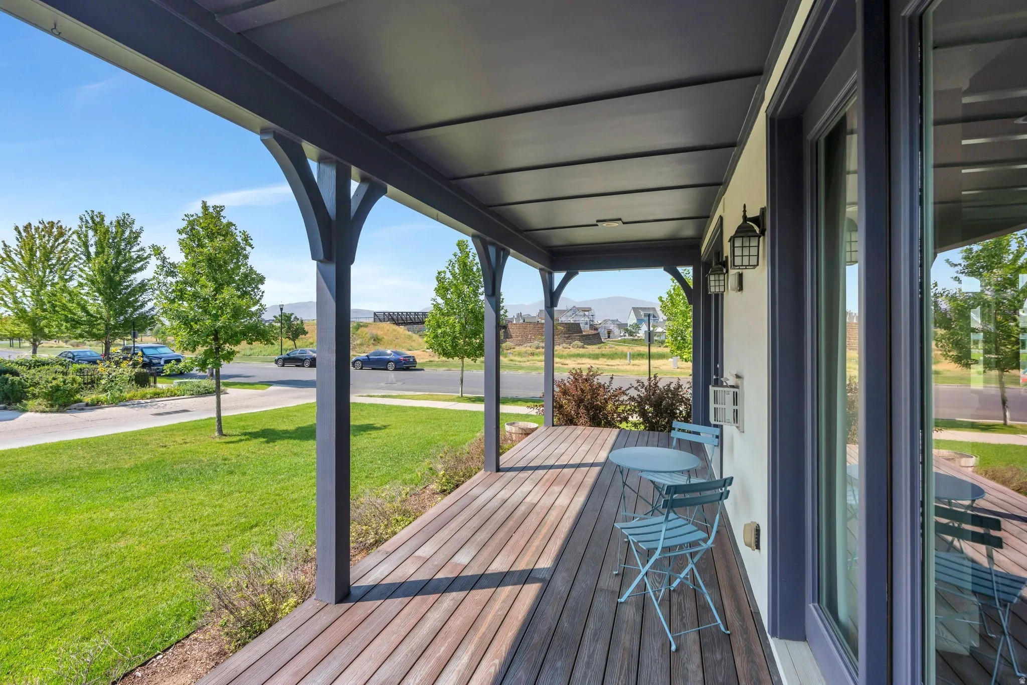Covered porch with wood-finish decking, dark-toned support columns, and two wall-mounted lanterns