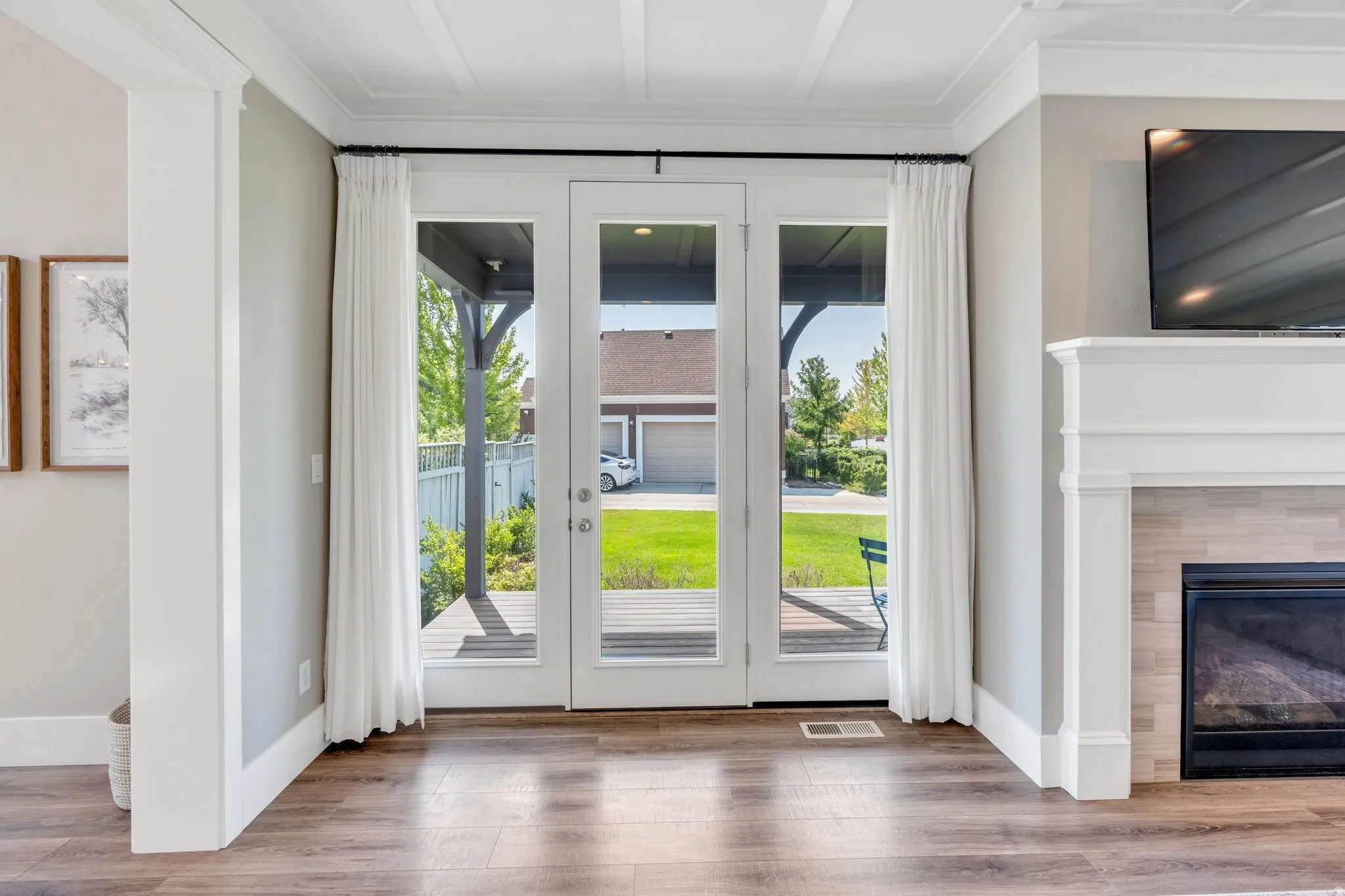 Wood-finish flooring, white coffered ceiling, a fireplace with a white mantel and tile surround, and French doors leading to an exterior deck