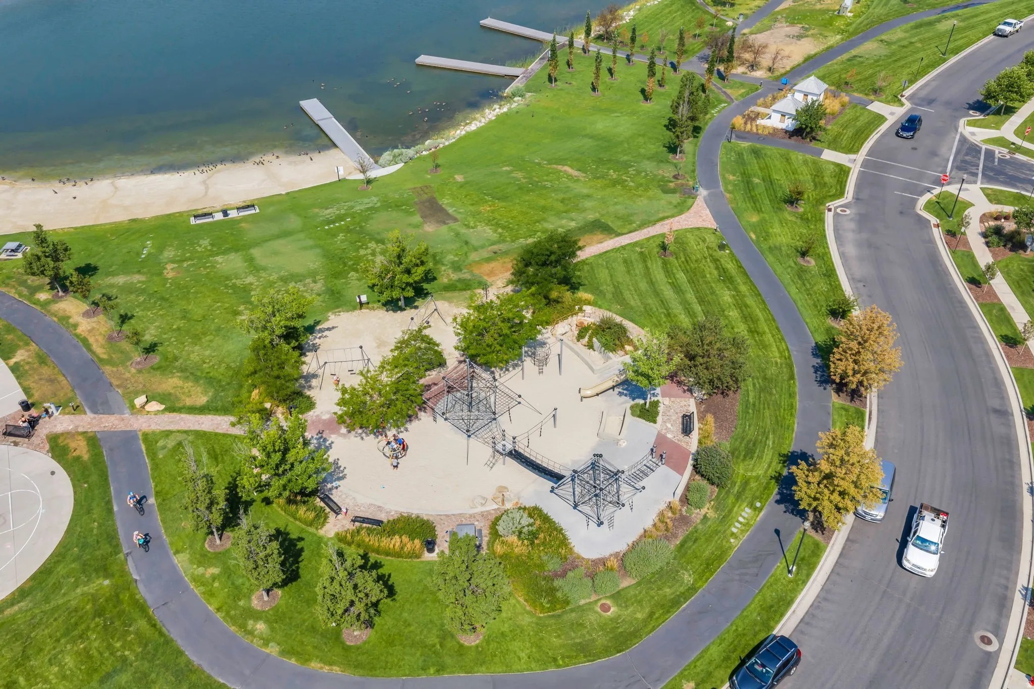 Expansive green spaces featuring a sand-based playground, paved walking paths, and mature trees