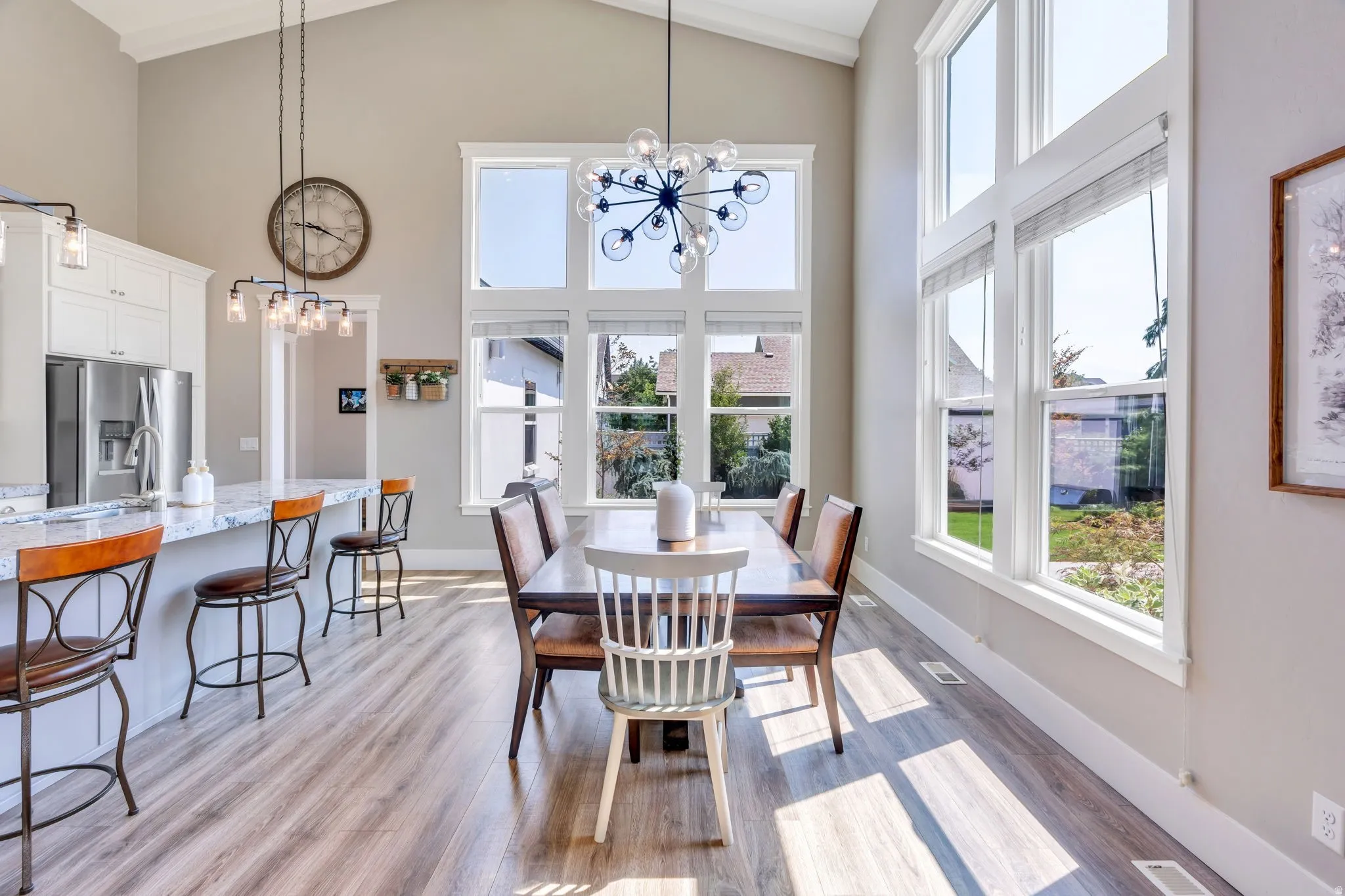 Vaulted ceiling, expansive windows, wood-finish flooring, white cabinetry, and stainless steel appliances