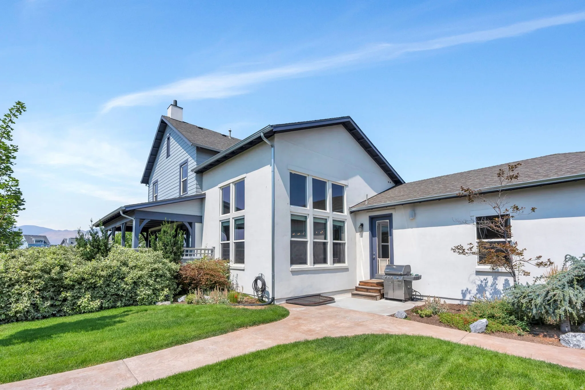 Stucco and siding exterior with multiple window configurations, a covered porch, and a concrete patio