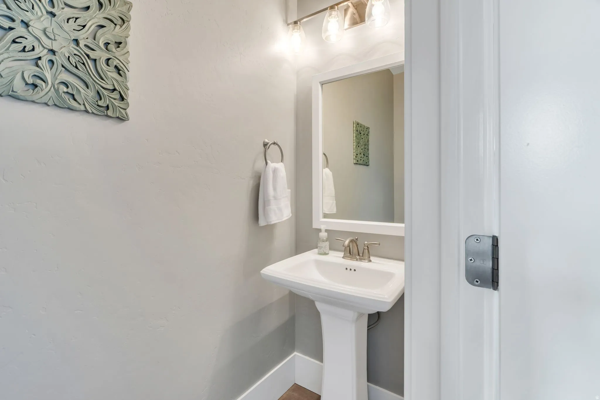 Pedestal sink with a brushed nickel faucet, framed mirror, and integrated vanity lighting