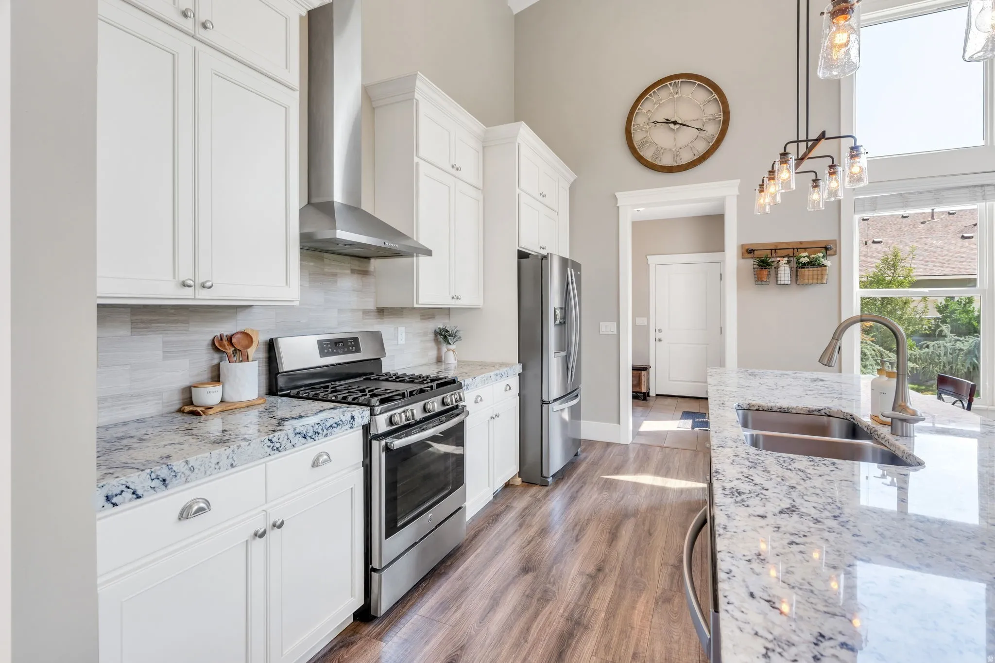 Gourmet kitchen featuring white cabinetry, stainless steel appliances, speckled countertops, wood-finish flooring, and a large window