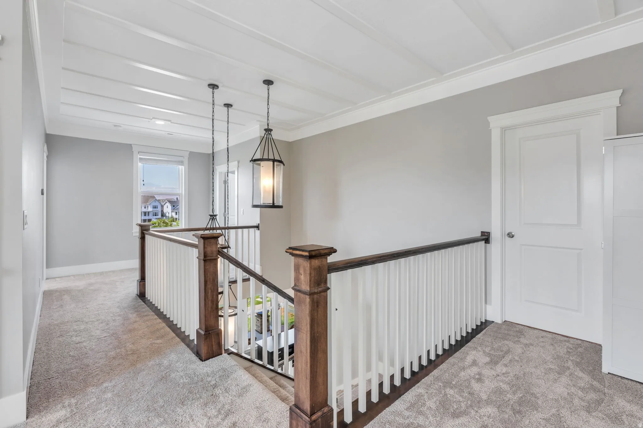 Coffered ceiling with recessed lighting, two-tone staircase railing with dark wood newel posts, and neutral-toned carpeting