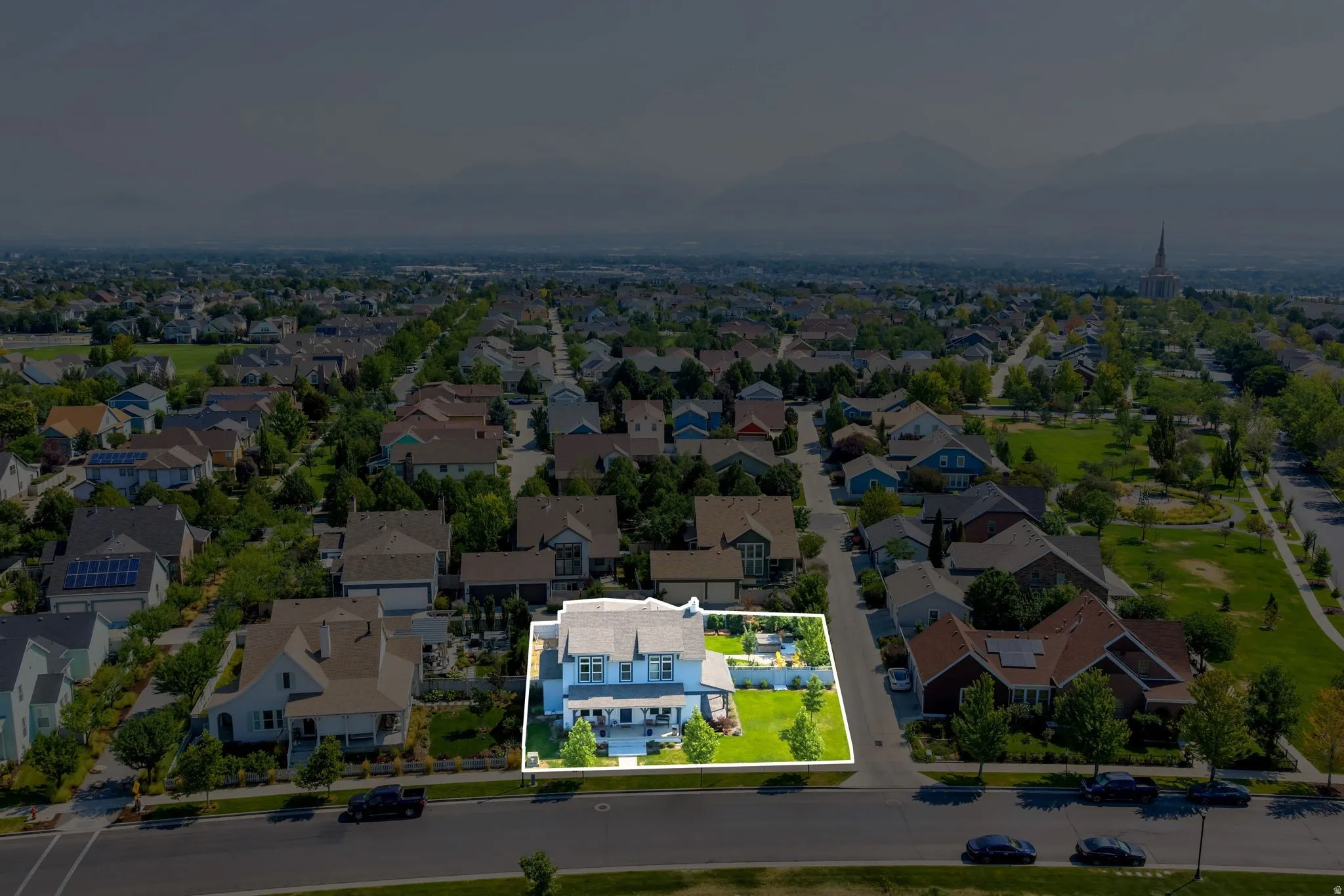 Aerial overview of the property featuring a light-colored exterior, an expansive manicured lawn, established landscaping, and a paved driveway