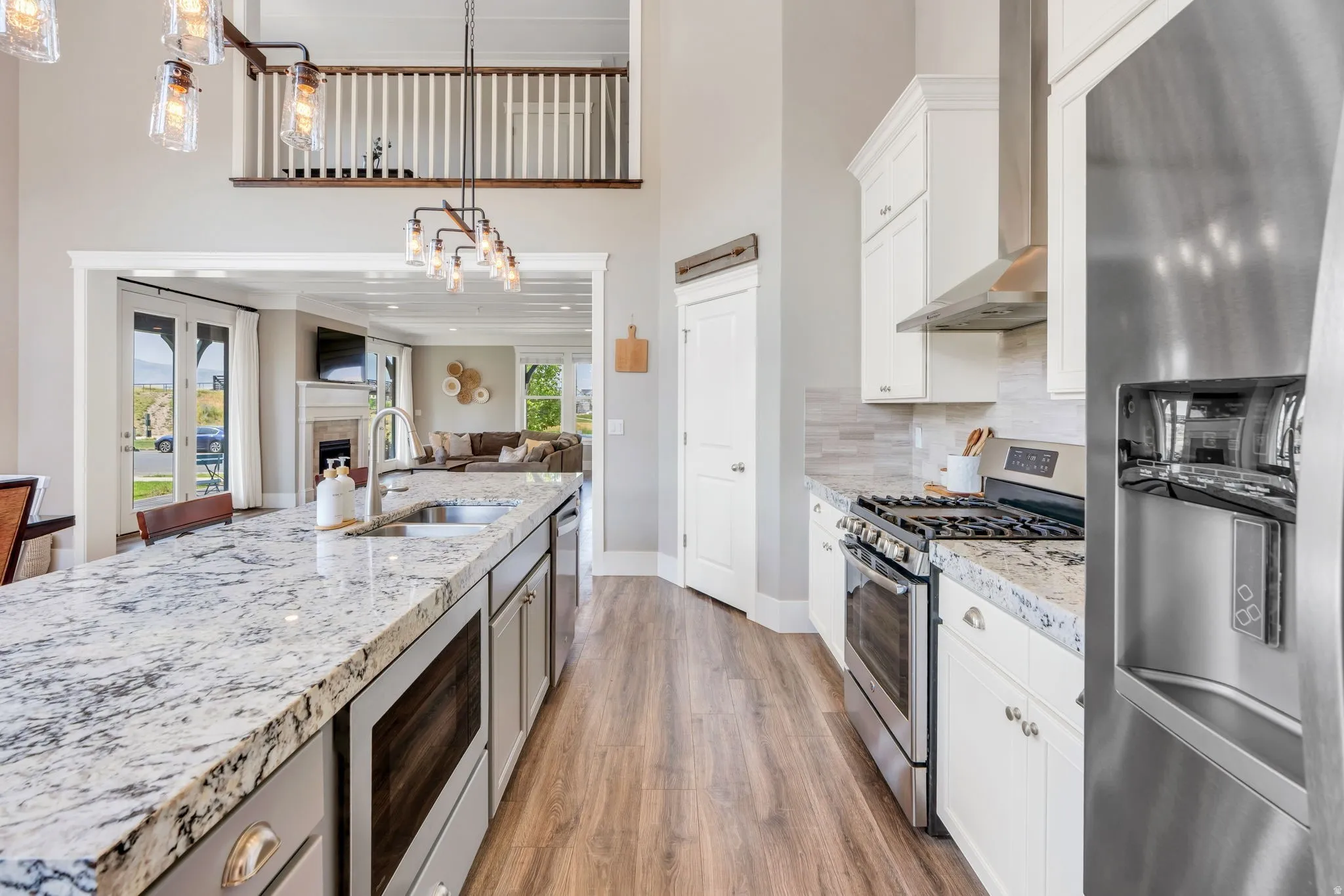 Spacious kitchen featuring a large island, stainless steel appliances, wood-finish flooring, white cabinetry, and a tile backsplash