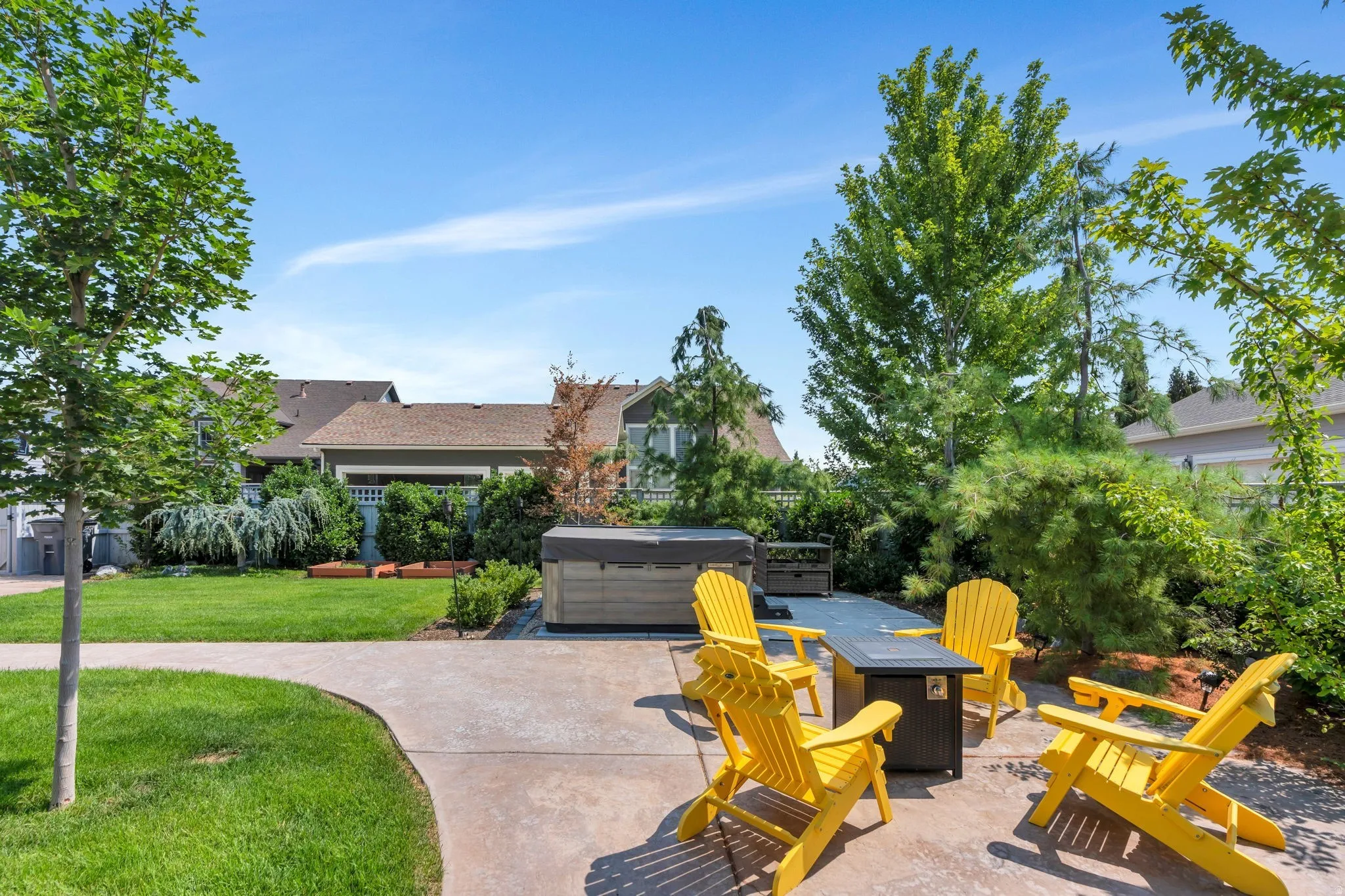 Paved patio area, built-in hot tub, concrete pathway, manicured lawn, and mature trees
