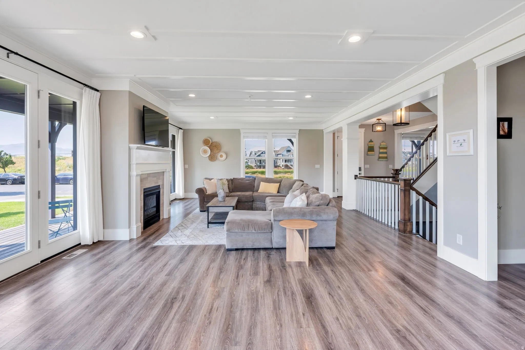 Open-concept living space featuring wood-finish flooring, a fireplace with a stone surround, recessed lighting, and a staircase with white spindles and a wood handrail