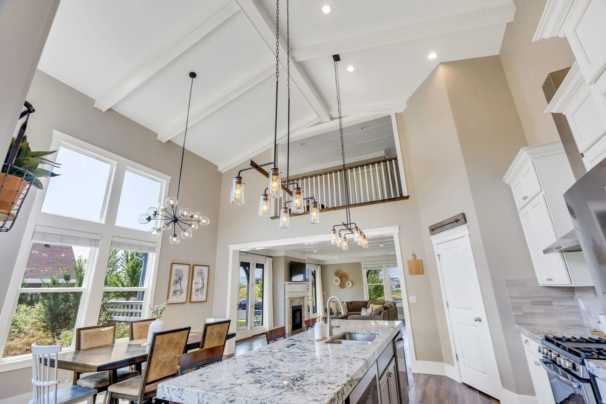 Vaulted ceiling with exposed beams, open-concept design, kitchen island with integrated sink, stainless steel appliances, and large windows
