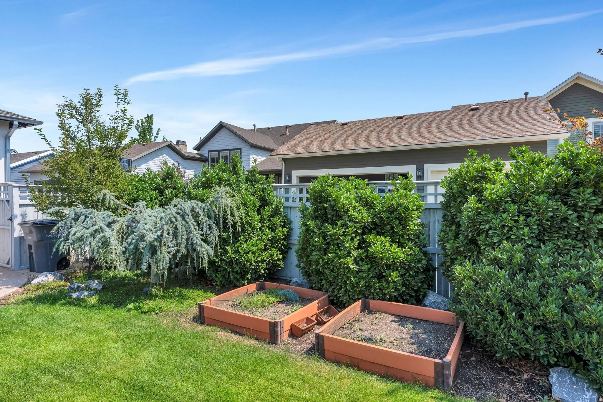 Landscaped yard featuring a manicured lawn, established shrubs, and two raised garden beds