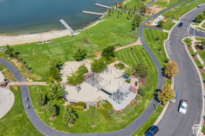 Expansive green space featuring a large playground with sand surfacing, paved walking paths, open grassy areas, and proximity to a body of water with docks