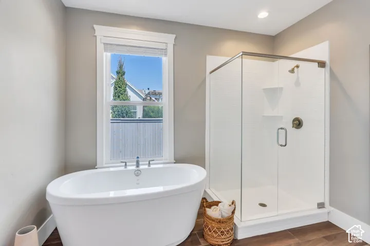 Freestanding oval soaking tub, glass-enclosed shower with white subway tile surround, wood-finish flooring, and a single window with white trim