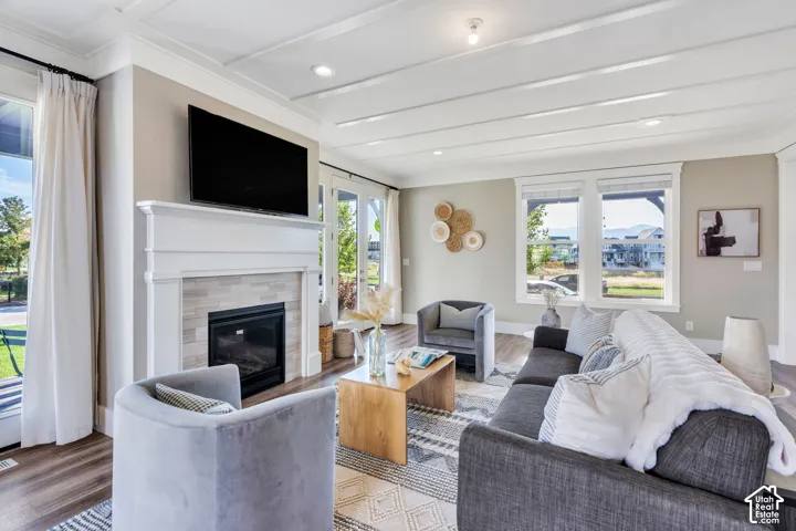Bright, open living area featuring a fireplace with white surround and black insert, wall-mounted flat-screen television, wood-finish flooring, recessed ceiling lighting, and multiple large windows with natural light and water views