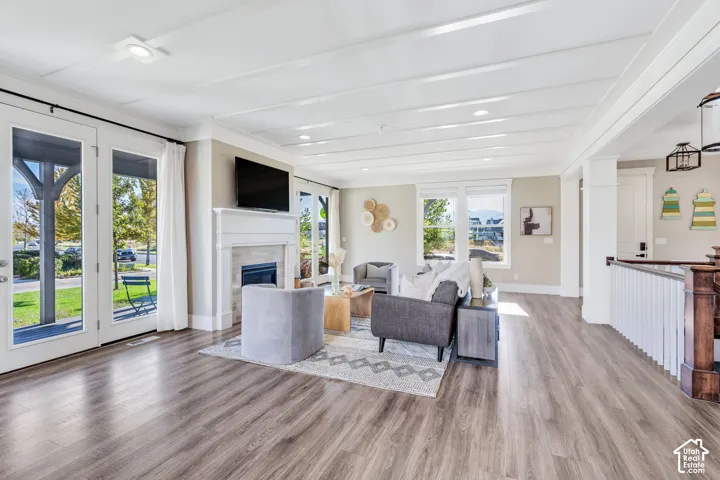 Wood-finish flooring throughout, living room featuring a fireplace with a stone surround and white mantel, two sets of French doors, and a decorative coffered ceiling