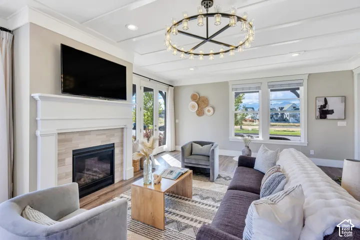 Living area featuring a coffered ceiling, oversized circular chandelier, fireplace with horizontal tile surround and custom mantel, wood-finish flooring, and large windows with mountain scenery
