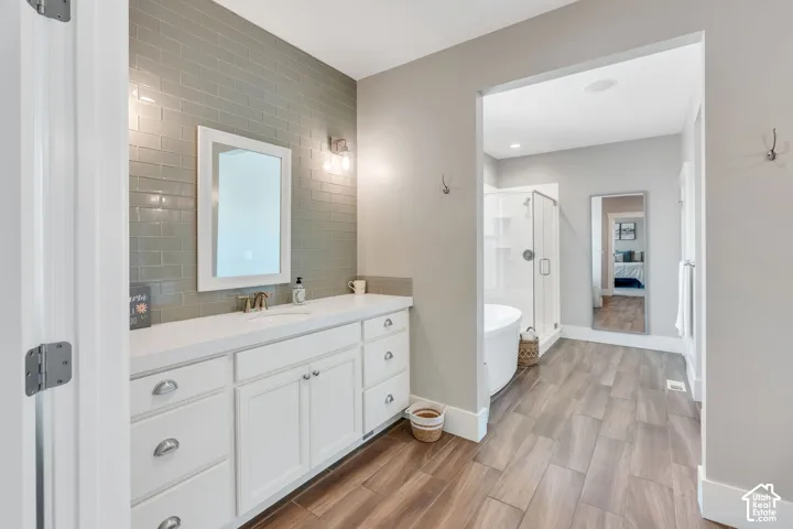 Spa-inspired primary bathroom featuring a white shaker-style vanity with multiple drawers and chrome hardware, a rectangular illuminated mirror, and subway tile accent wall
