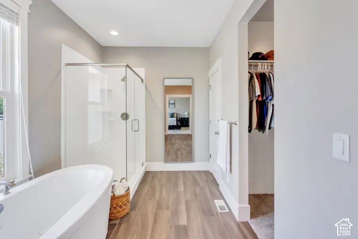 Freestanding soaking tub, glass-enclosed shower, wood-finish flooring, and recessed lighting