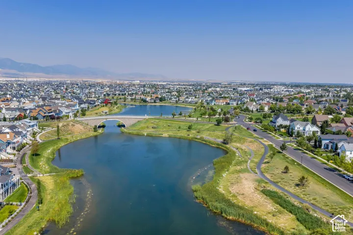 Aerial perspective featuring multiple lakes, a stone arch bridge, meandering paved pathways, and an expansive residential development