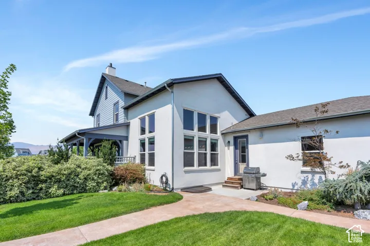 Exterior featuring a stucco finish with siding accents, expansive windows, a covered porch, a concrete patio, and a manicured lawn