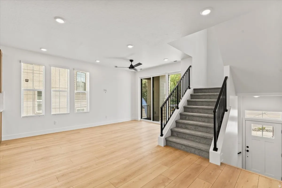 Light wood-finish flooring, recessed ceiling lighting, three tall windows with blinds, a ceiling fan, and sliding glass doors