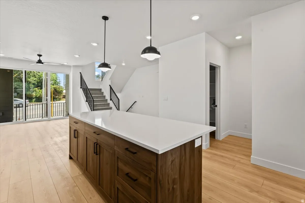 Kitchen island with ample storage, light wood-finish flooring, recessed lighting, and a contemporary staircase with black railings