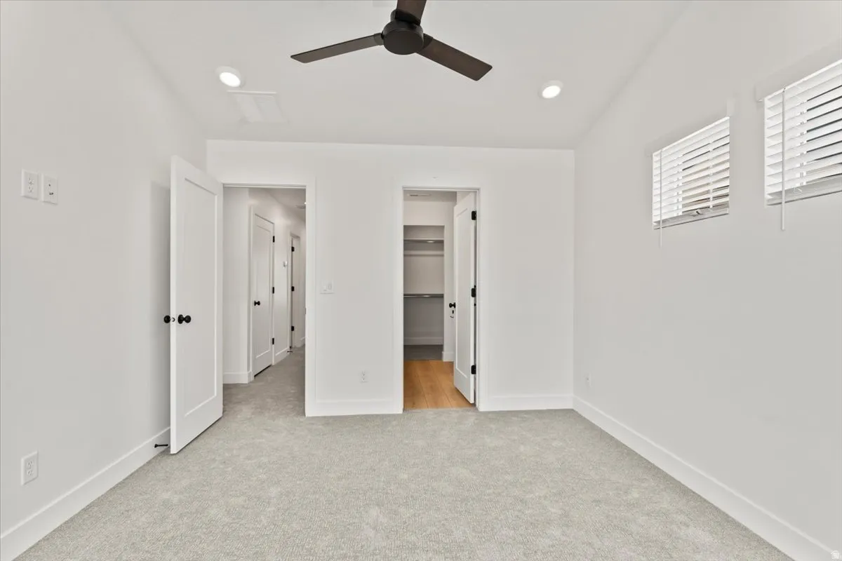 Recessed lighting, ceiling fan, two windows with blinds, light-colored carpeting, and white walls