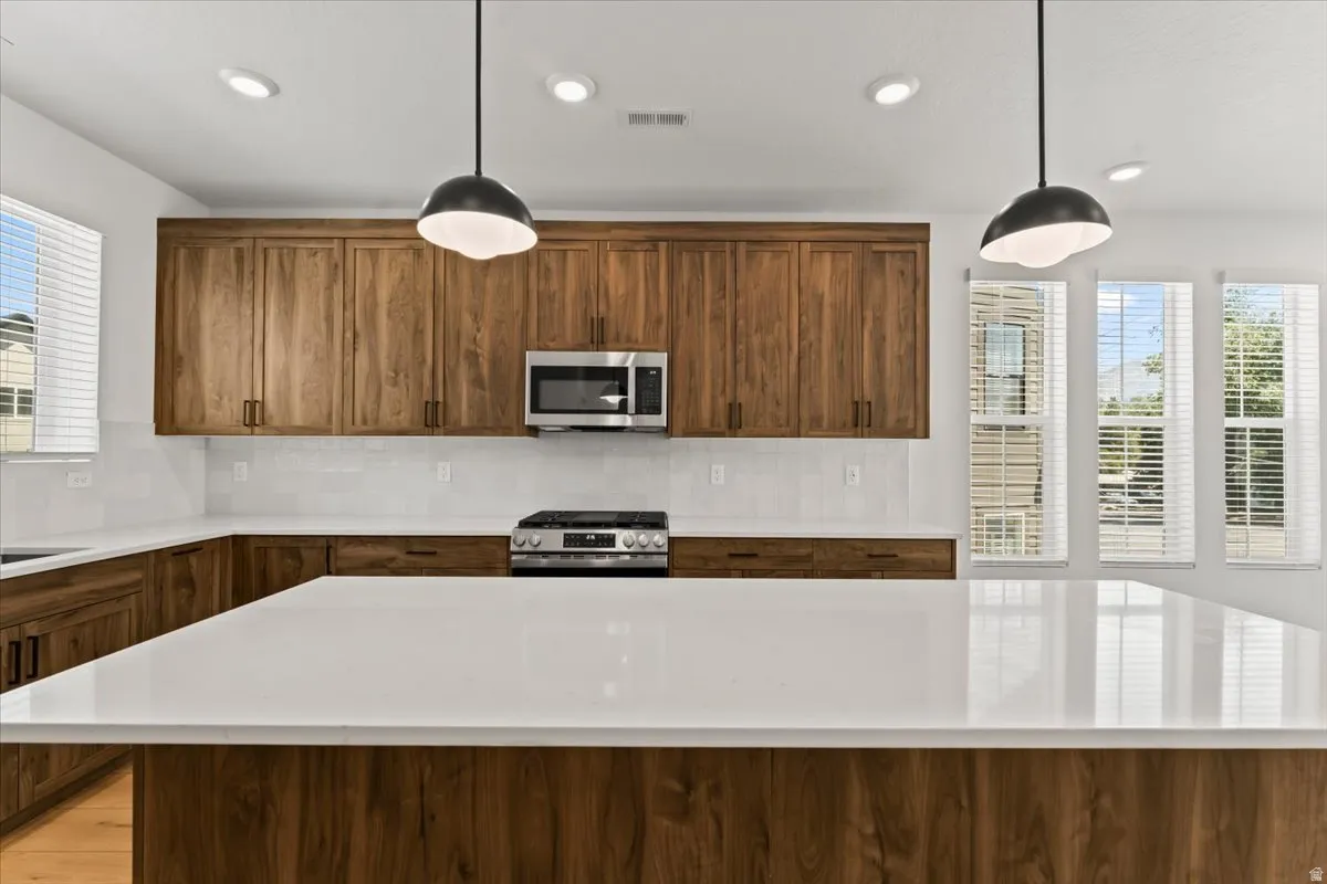 Kitchen featuring a large center island, wood-finish cabinetry, stainless steel appliances, a tile backsplash, and recessed lighting