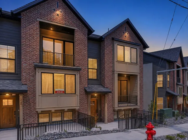 Brick and dark siding exterior with prominent gabled rooflines, upper-level balconies with black railings, and a ground-level ramp leading to the entrance