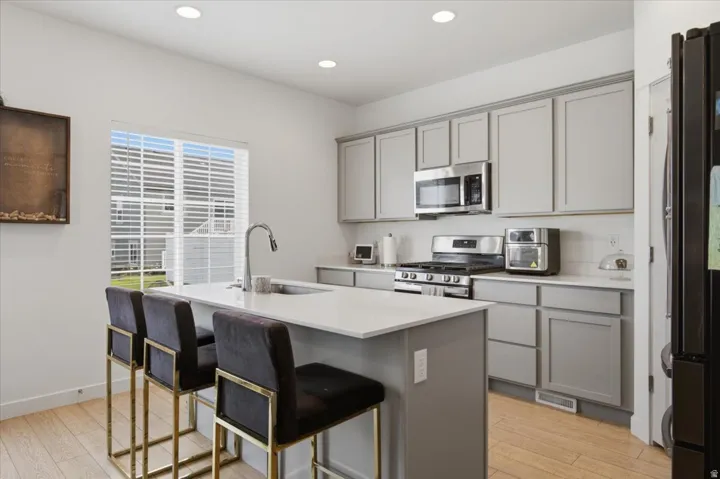 Kitchen featuring a central island with an integrated sink, light wood-finish flooring, recessed lighting, and light gray cabinetry