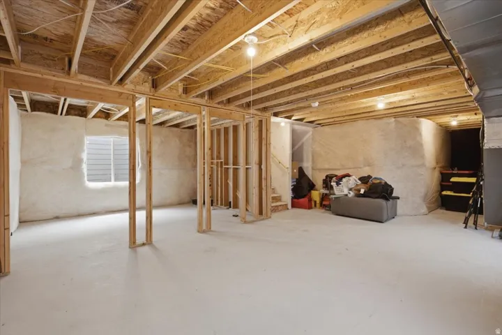 Unfinished lower level featuring exposed wood framing, wood joists, and a single window. Plumbing is stubbed-in.