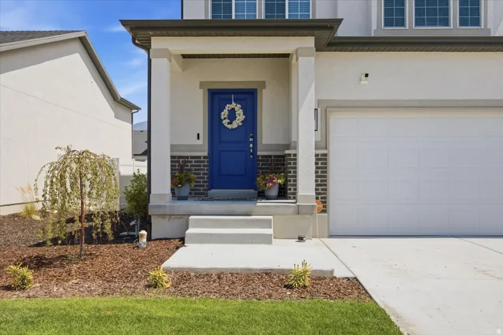 Stucco exterior with a prominent blue entry door, an integrated two-car garage, concrete entry stairs, and a covered porch