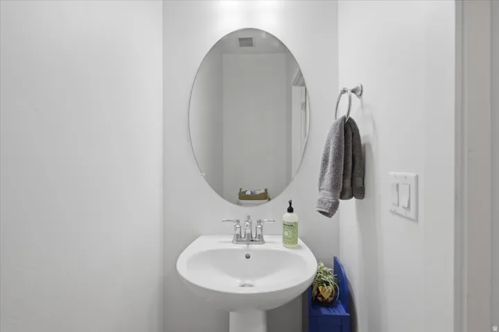 Pedestal sink with a polished chrome faucet, oval wall mirror, and a wall-mounted towel ring