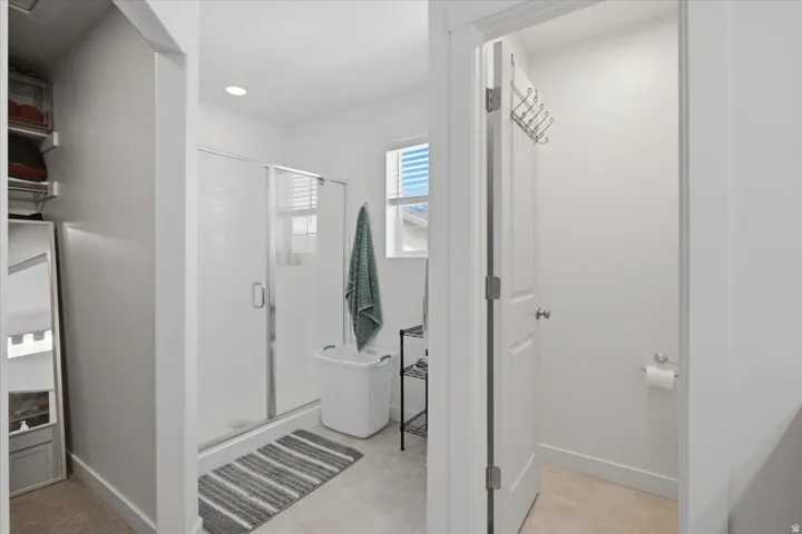 Master bathroom with glass-enclosed shower, window with blinds, recessed lighting, and built-in closet shelving