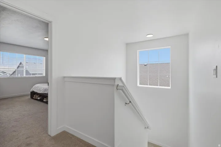 Carpeted hallway with a staircase, featuring a white painted handrail and trim, recessed lighting, and window