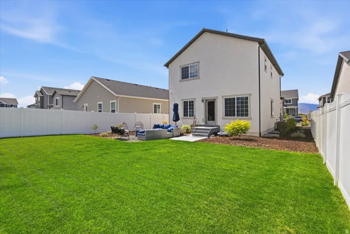 Expansive green lawn, white privacy fencing, concrete patio area, rear entrance, and exterior lighting