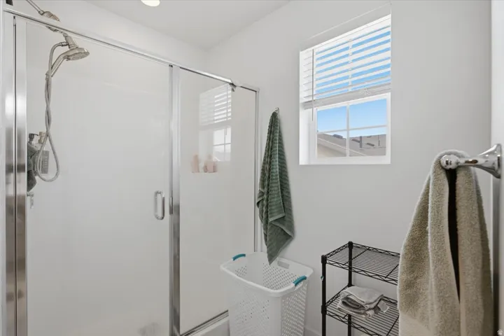 Mater bathroom with glass-enclosed shower with a multi-function showerhead, bright window with blinds, and recessed lighting
