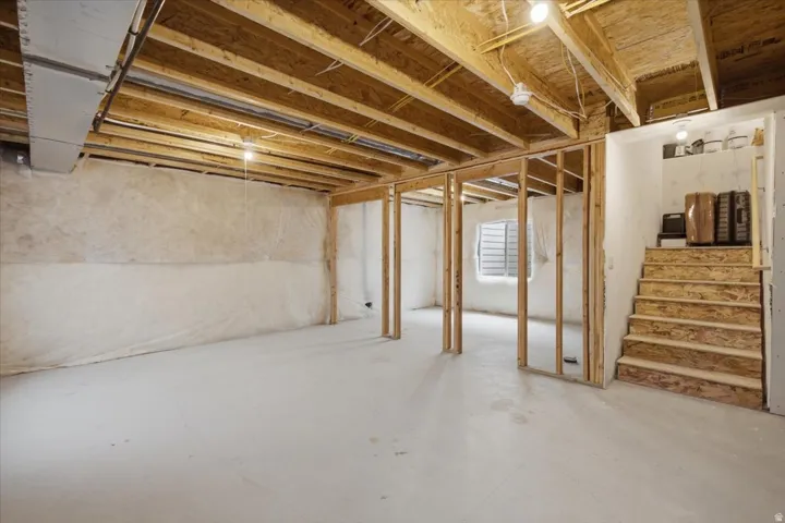 Unfinished lower level with wood framing, exposed ceiling joists, and a window. Plumbing is stubbed-in.