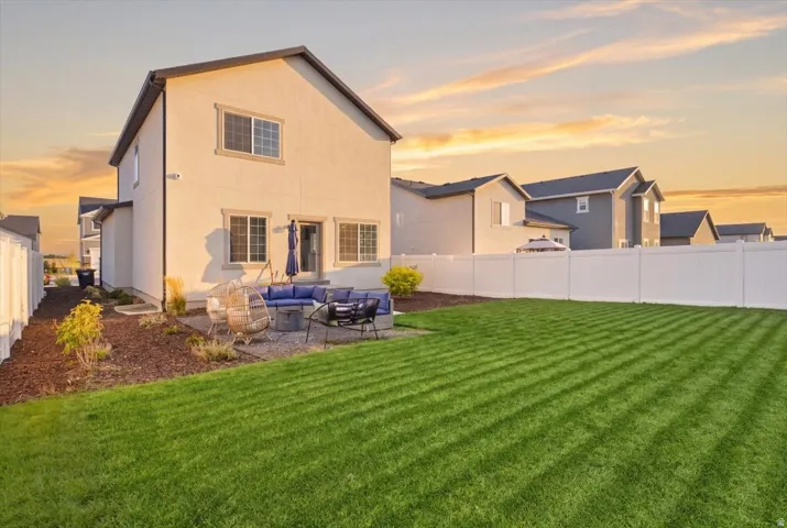Expansive backyard featuring a manicured lawn, white privacy fencing, and a gravel patio area